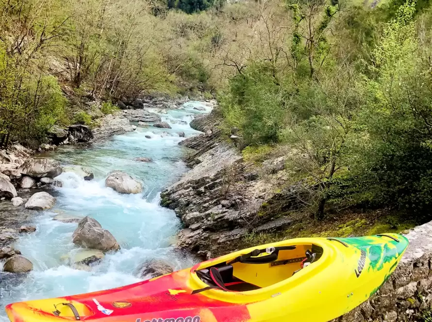 A kayak lays on the ground next to a river.