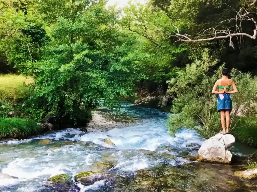 A woman practices yoga on top of a river boulder in Greece