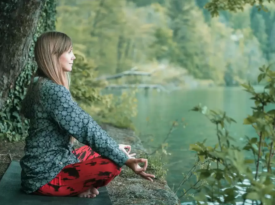 A woman meditates next to a river