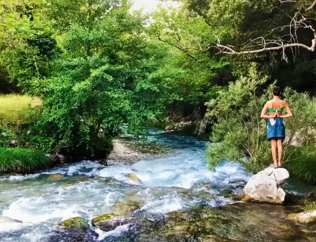 A woman practices yoga on top of a river boulder in Greece