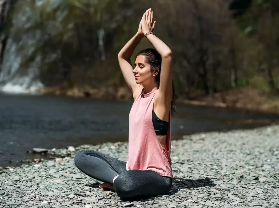 A woman practices yoga next to a river.