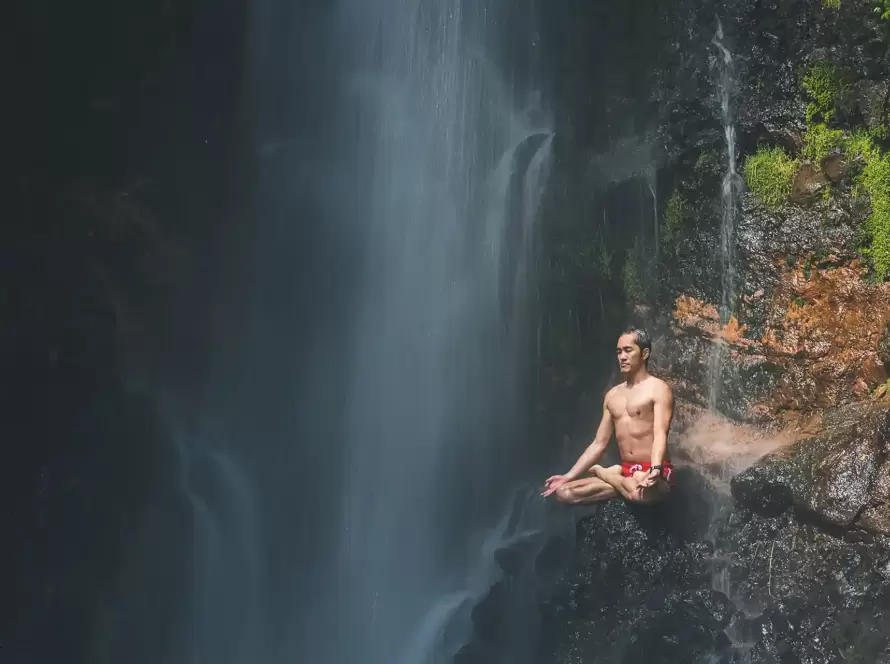 A man meditates next to a waterfall