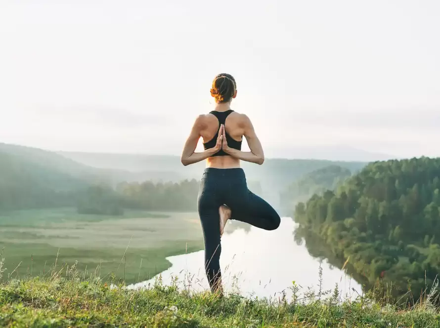 A woman practices yoga overlooking a beautiful scenic river view.