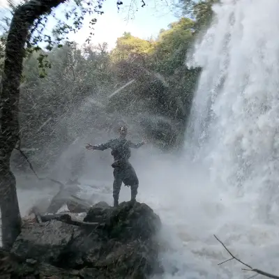 A person stands next to a waterfall in Greece