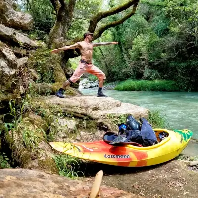 A man practices yoga next to a river in Greece with a kayak in the foreground
